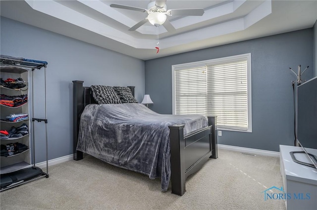 bedroom with light colored carpet, a raised ceiling, and ceiling fan