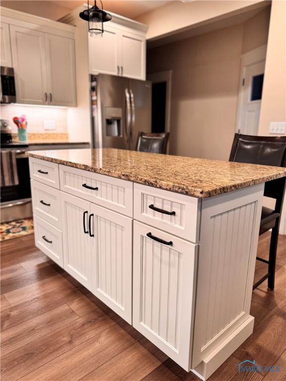 kitchen with light stone countertops, a kitchen breakfast bar, stainless steel appliances, white cabinets, and a kitchen island