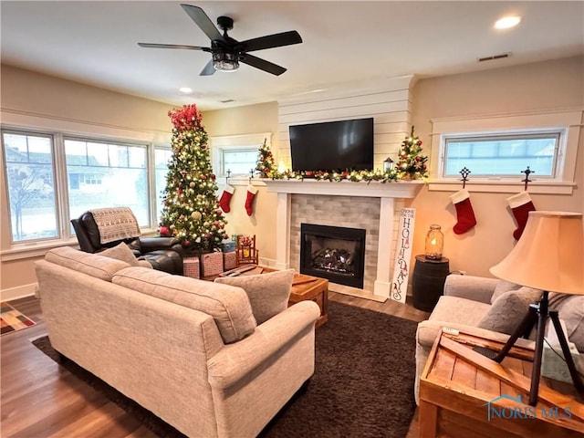 living room with a healthy amount of sunlight, ceiling fan, dark wood-type flooring, and a tiled fireplace