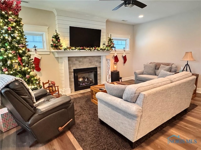 living room featuring ceiling fan, a fireplace, and dark wood-type flooring