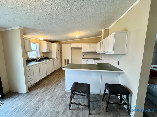 kitchen featuring kitchen peninsula, sink, a breakfast bar area, white cabinetry, and lofted ceiling