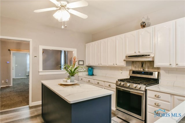 kitchen with light stone countertops, gas range, white cabinets, a center island, and light hardwood / wood-style floors