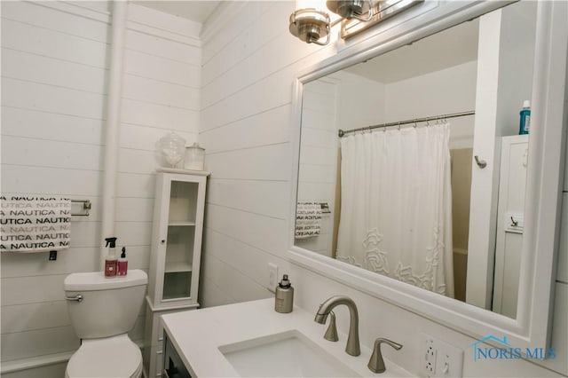 bathroom featuring vanity, wood walls, a shower with shower curtain, and toilet