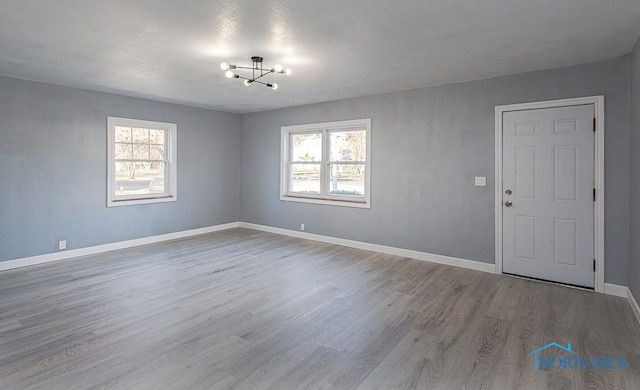 empty room with a chandelier, light wood-type flooring, and a wealth of natural light