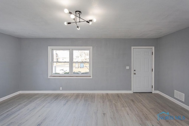 unfurnished room featuring a chandelier and light hardwood / wood-style floors