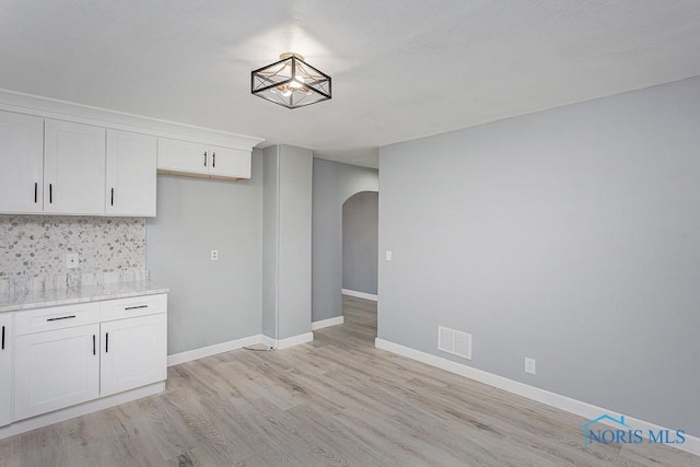 kitchen with tasteful backsplash, white cabinetry, light hardwood / wood-style flooring, and light stone counters