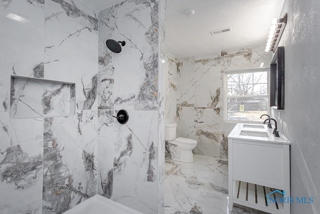 bathroom featuring vanity, toilet, a tile shower, and tile walls