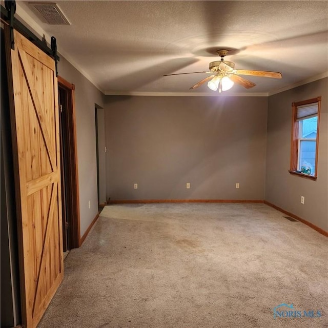 carpeted empty room featuring a textured ceiling, a barn door, ceiling fan, and crown molding