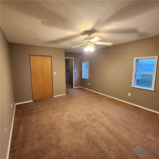 unfurnished bedroom with ceiling fan, a textured ceiling, and dark colored carpet