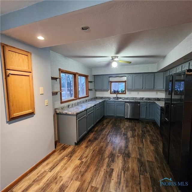 kitchen featuring light stone countertops, black refrigerator, ceiling fan, dark wood-type flooring, and dishwasher