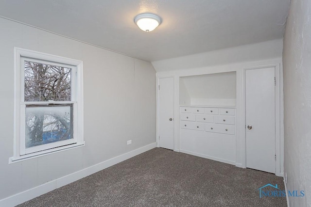 unfurnished bedroom featuring lofted ceiling and dark colored carpet