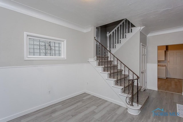 stairs featuring wood-type flooring and crown molding