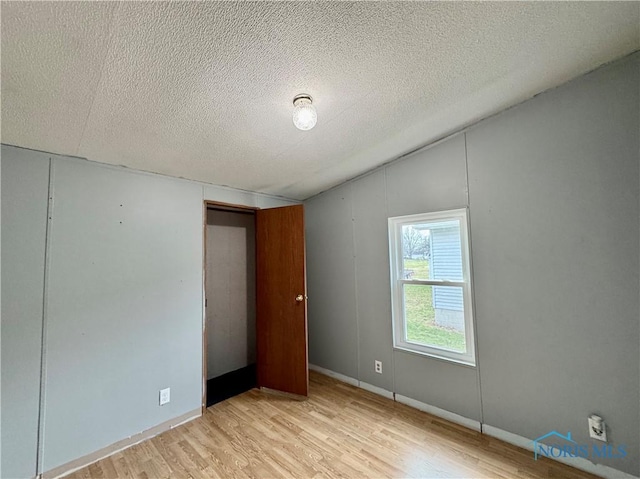 empty room featuring a textured ceiling, light hardwood / wood-style flooring, and lofted ceiling