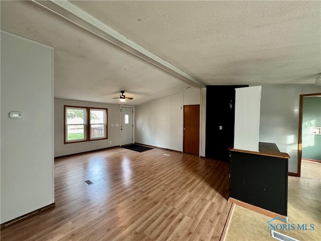 unfurnished living room featuring a textured ceiling, vaulted ceiling with beams, light hardwood / wood-style flooring, and ceiling fan