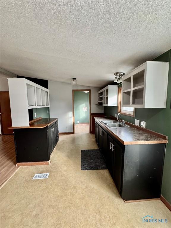 kitchen with a textured ceiling, ceiling fan, sink, white cabinets, and a kitchen island