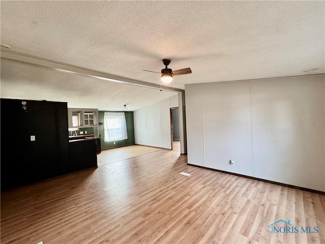 unfurnished living room with ceiling fan, light hardwood / wood-style flooring, and a textured ceiling