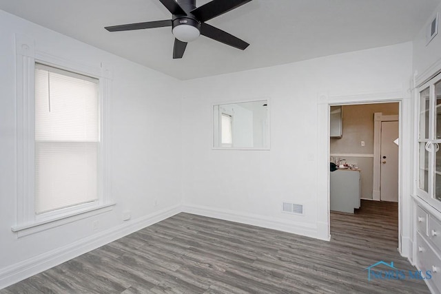 empty room with ceiling fan, a healthy amount of sunlight, and dark wood-type flooring