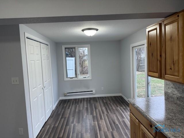 unfurnished dining area featuring a healthy amount of sunlight, dark wood-type flooring, and a baseboard heating unit