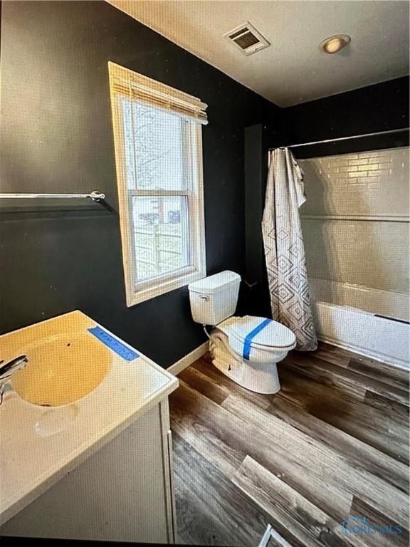 full bathroom featuring hardwood / wood-style floors, vanity, shower / bath combination with curtain, and toilet