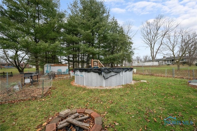 view of yard with fence, a covered pool, an outdoor structure, a storage unit, and a fire pit