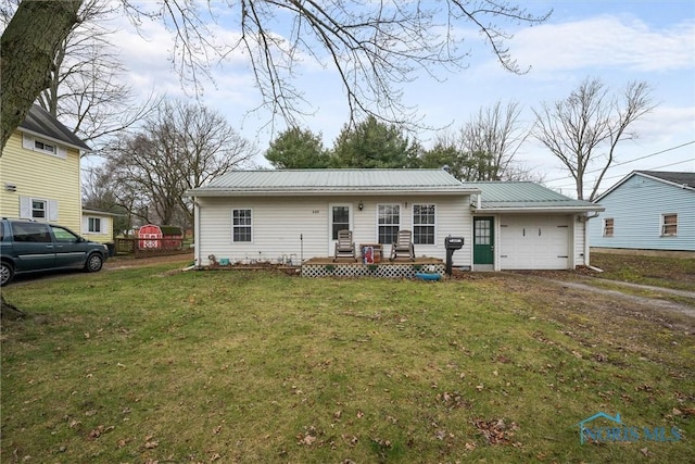 back of property featuring metal roof, driveway, a garage, and a yard
