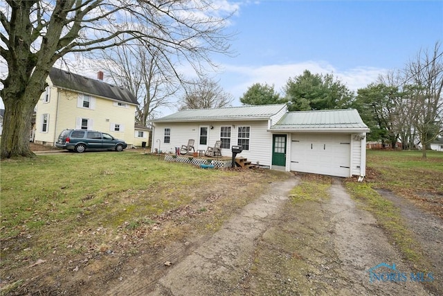 back of house with metal roof, an attached garage, driveway, and a lawn