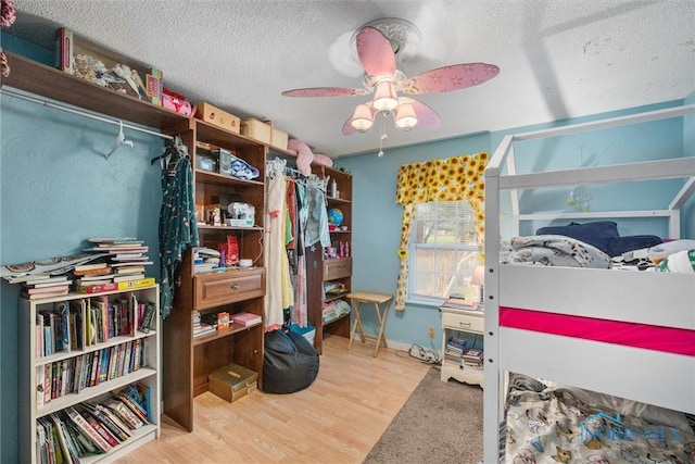 bedroom with ceiling fan, wood finished floors, and a textured ceiling