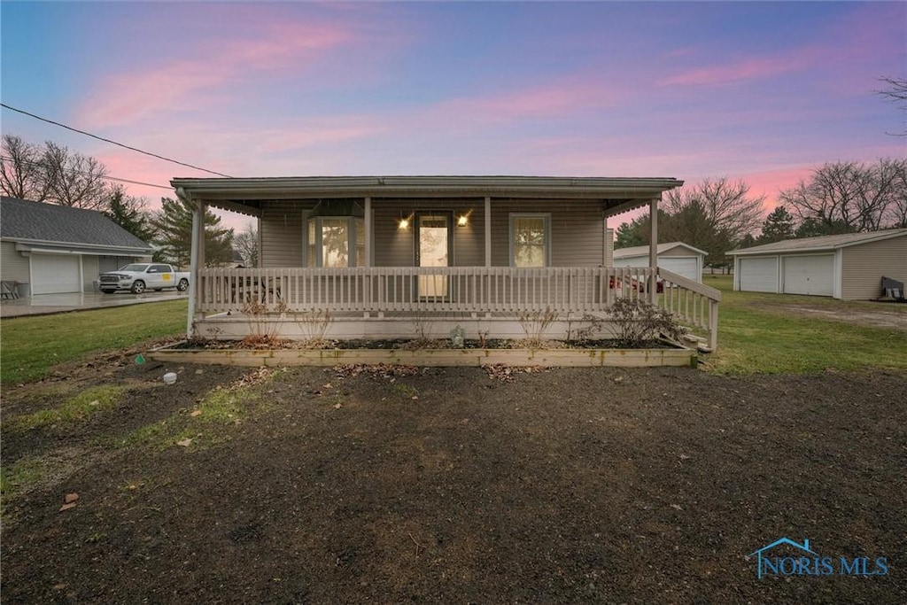 view of front facade featuring covered porch, an outbuilding, a garage, and a lawn