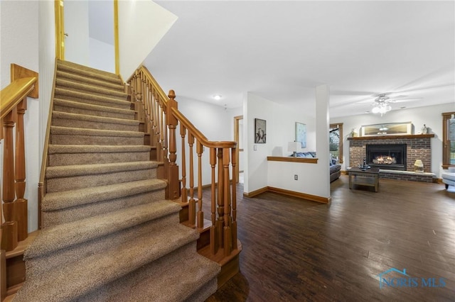 stairway with a fireplace, hardwood / wood-style floors, and ceiling fan