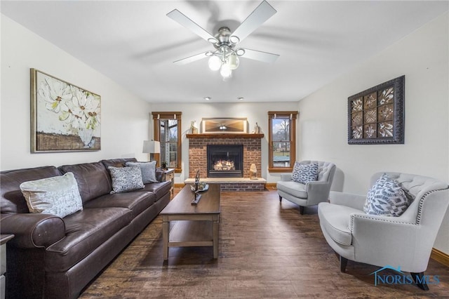 living room with a brick fireplace, ceiling fan, and dark wood-type flooring