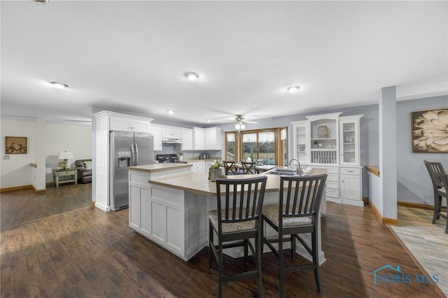 kitchen featuring stove, dark wood-type flooring, a center island with sink, white cabinets, and stainless steel fridge with ice dispenser