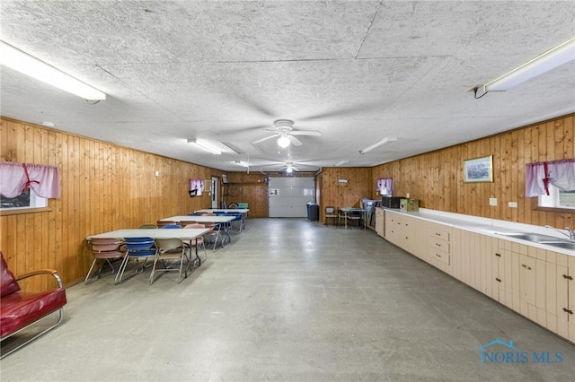 basement with a textured ceiling, ceiling fan, wood walls, and sink