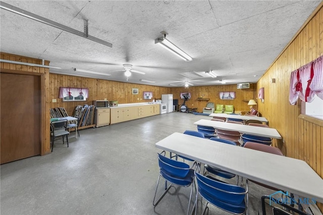 interior space with concrete flooring, a textured ceiling, ceiling fan, and wood walls