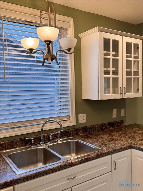 kitchen with a wealth of natural light, sink, white cabinets, and hanging light fixtures