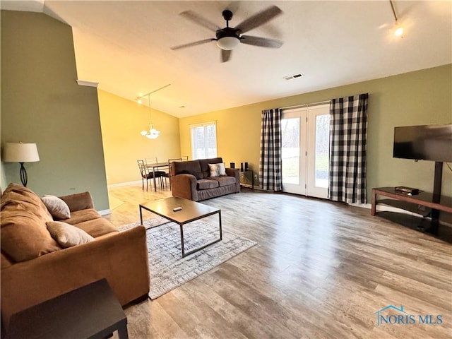 living room with ceiling fan with notable chandelier, wood-type flooring, and vaulted ceiling