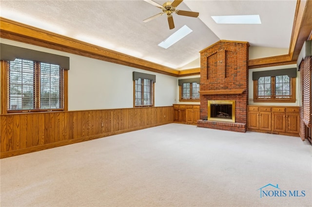 unfurnished living room with carpet flooring, ceiling fan, lofted ceiling with skylight, and a brick fireplace