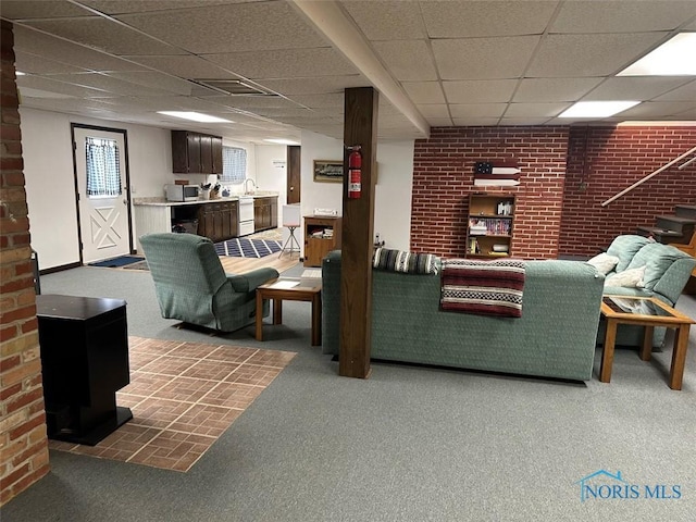 carpeted living room with a paneled ceiling, brick wall, and sink