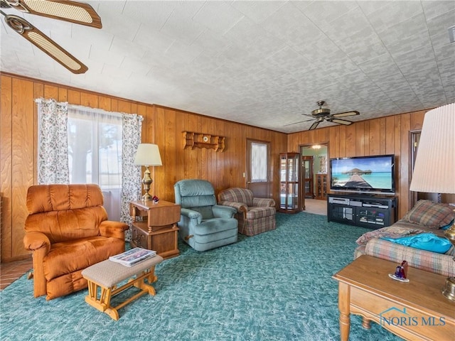 carpeted living room with ceiling fan and wood walls