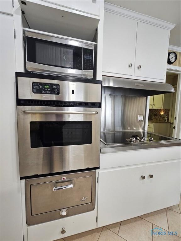 kitchen featuring exhaust hood, light tile patterned floors, appliances with stainless steel finishes, tasteful backsplash, and white cabinetry