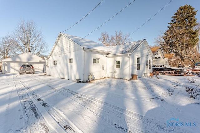 snow covered house with an outdoor structure and a garage