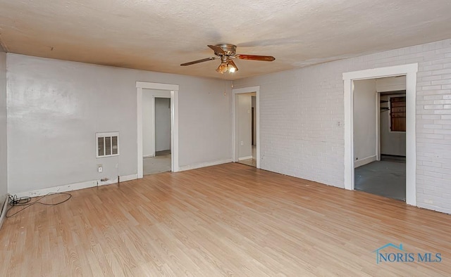 empty room with ceiling fan, brick wall, a textured ceiling, and light hardwood / wood-style flooring