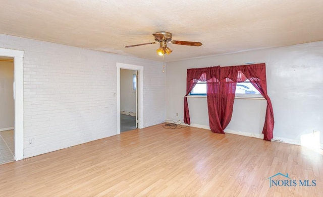 unfurnished room with hardwood / wood-style flooring, brick wall, and ceiling fan