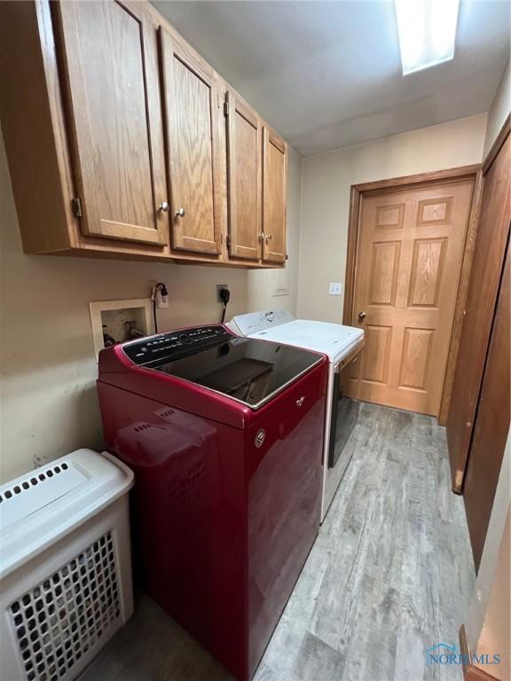 laundry area featuring cabinets, washing machine and dryer, and light hardwood / wood-style flooring