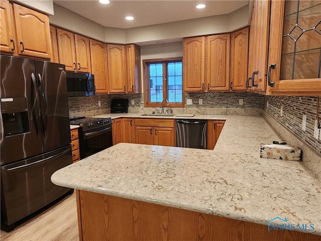 kitchen featuring backsplash, black appliances, sink, light stone counters, and kitchen peninsula