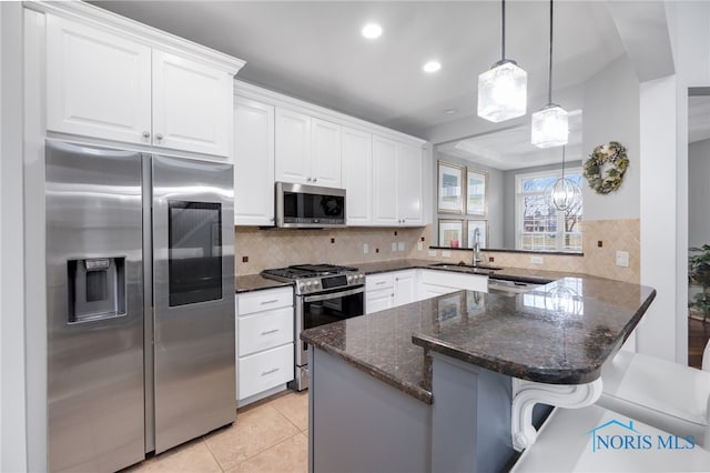 kitchen featuring a kitchen breakfast bar, stainless steel appliances, light tile patterned floors, dark stone countertops, and white cabinetry