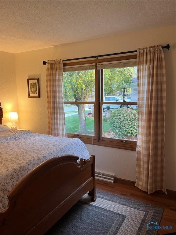 bedroom with wood-type flooring, a textured ceiling, and multiple windows