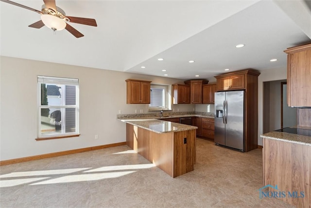 kitchen featuring stainless steel fridge, light stone counters, a breakfast bar, ceiling fan, and sink