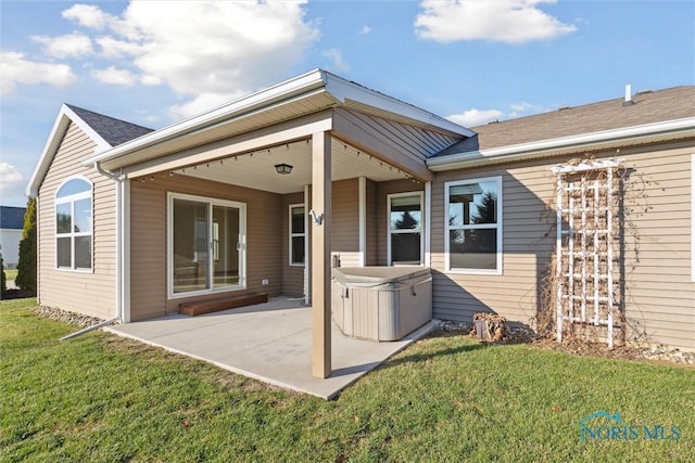 rear view of property with a lawn, a patio, and a hot tub