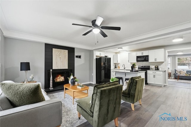 living room with ceiling fan, sink, a large fireplace, light wood-type flooring, and ornamental molding