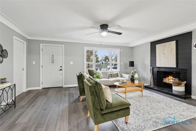 living room featuring crown molding, a large fireplace, ceiling fan, and hardwood / wood-style flooring